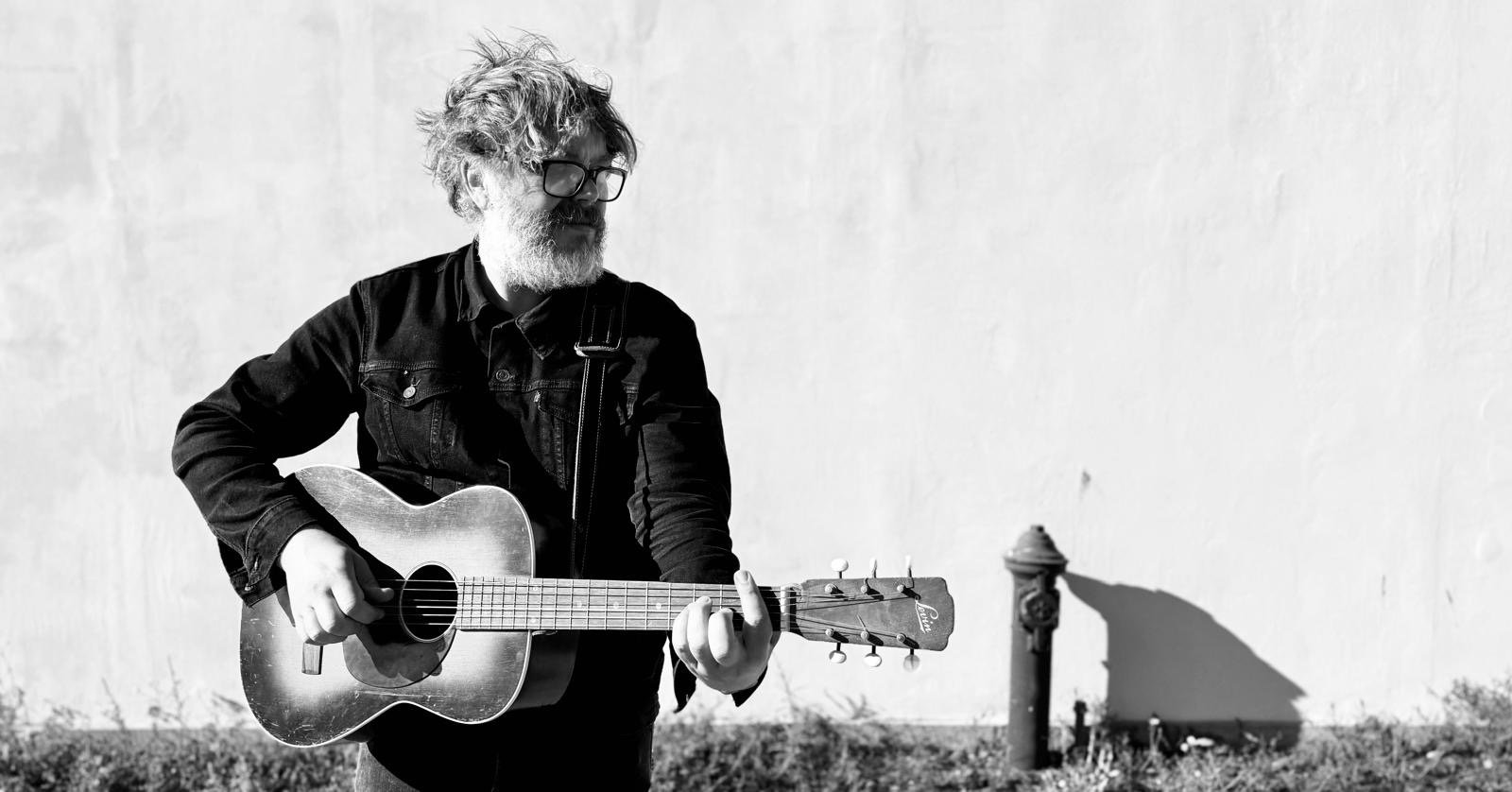 Elephant Moon portrait: playing acoustic guitar against a white wall